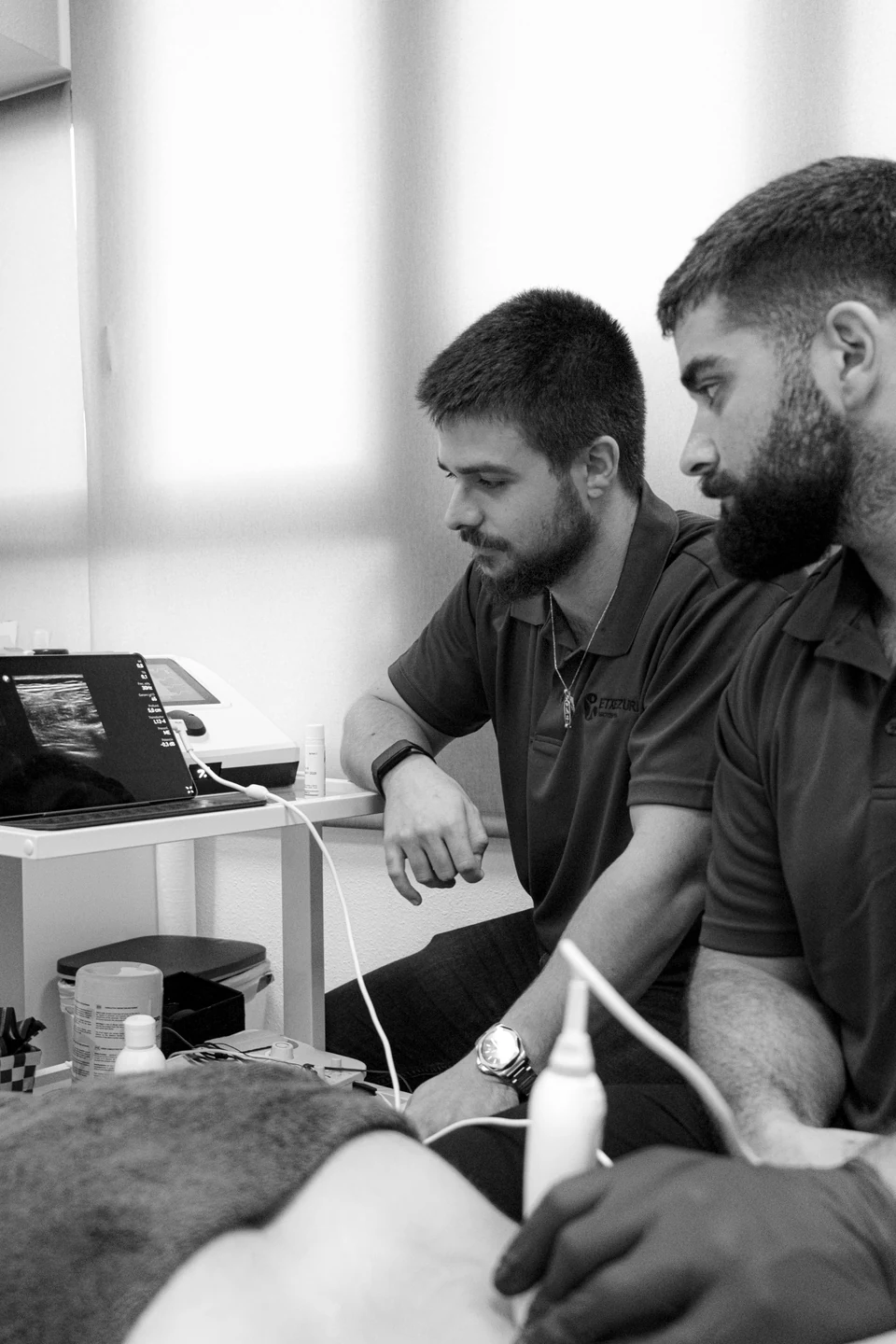 Iñigo Goikoetxea y Ander Blanco frente al ecógrafo durante una exploración con sonda; en blanco y negro