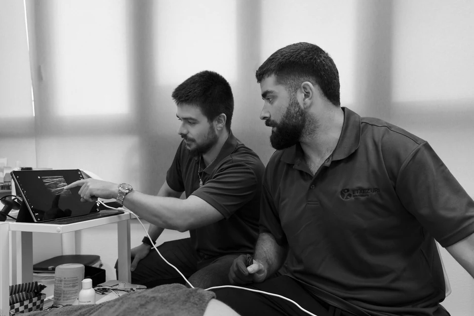 Iñigo Goikoetxea señala la pantalla del ecógrafo mientras Ander Blanco la observa; en blanco y negro
