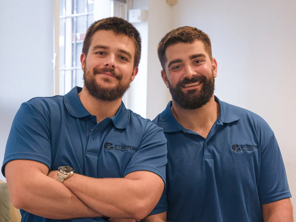 Iñigo Goikoetxea y Ander Blanco, fisioterapeutas de Etxezuri, sonríen a cámara con el polo azul de la clínica