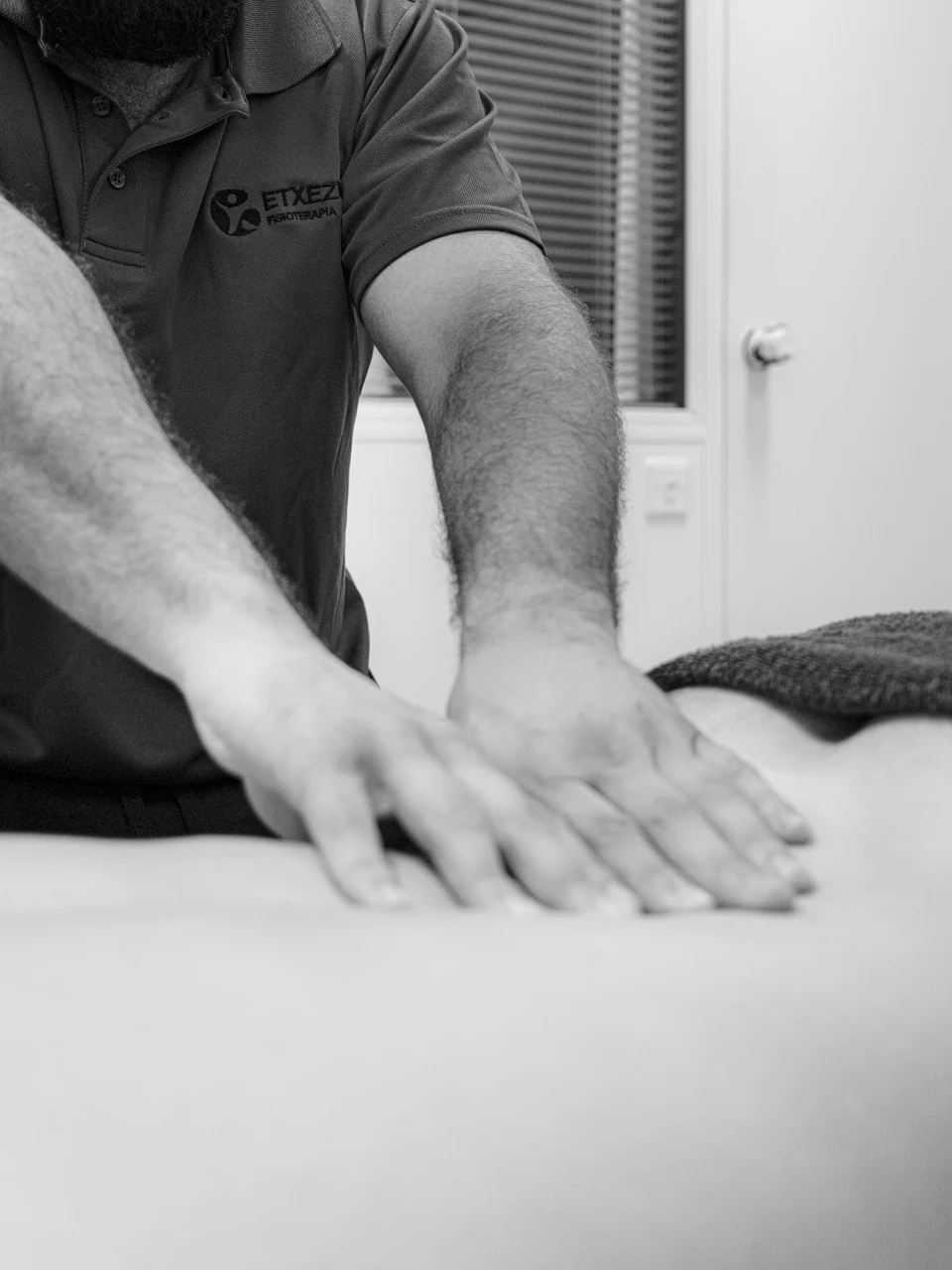 Detalle de las manos de Ander Blanco trabajando la espalda de un paciente; en blanco y negro