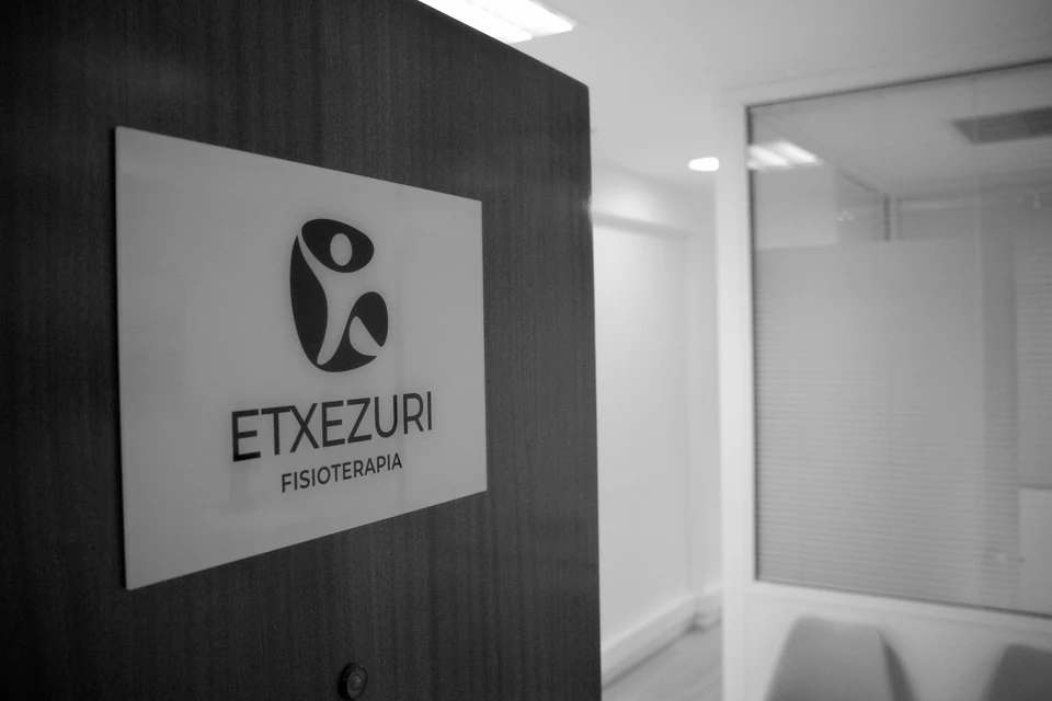 Placa con el logotipo de Etxezuri Fisioterapia en la puerta de madera de la clínica, en blanco y negro