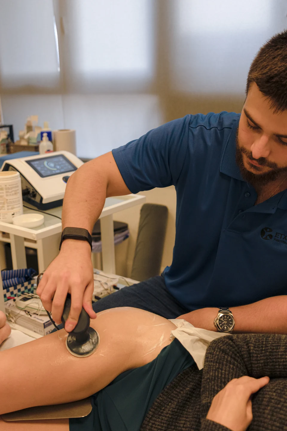Iñigo Goikoetxea aplica un cabezal con crema sobre la pierna de una paciente, con el equipo de terapia y el material de la sala detrás