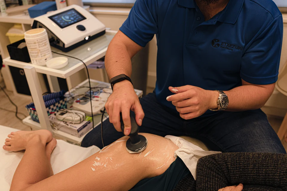 Cabezal de radiofrecuencia sobre el muslo de una paciente, con el equipo de electroterapia y el gel en el carro de al lado